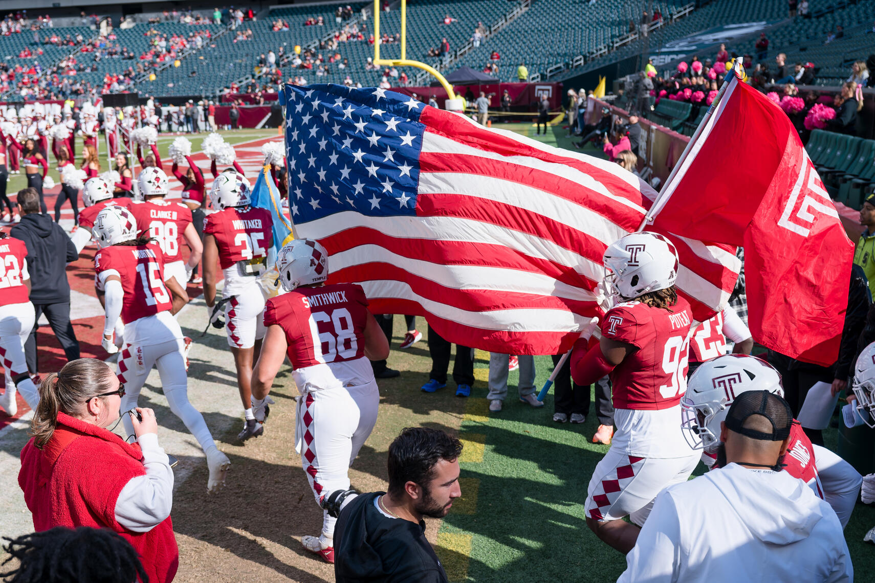PHILADELPHIA, PA - Temple Owls players run onto the field carrying team and American flags during pre‑game introductions before a 2025 NCAA football matchup at Lincoln Financial Field.